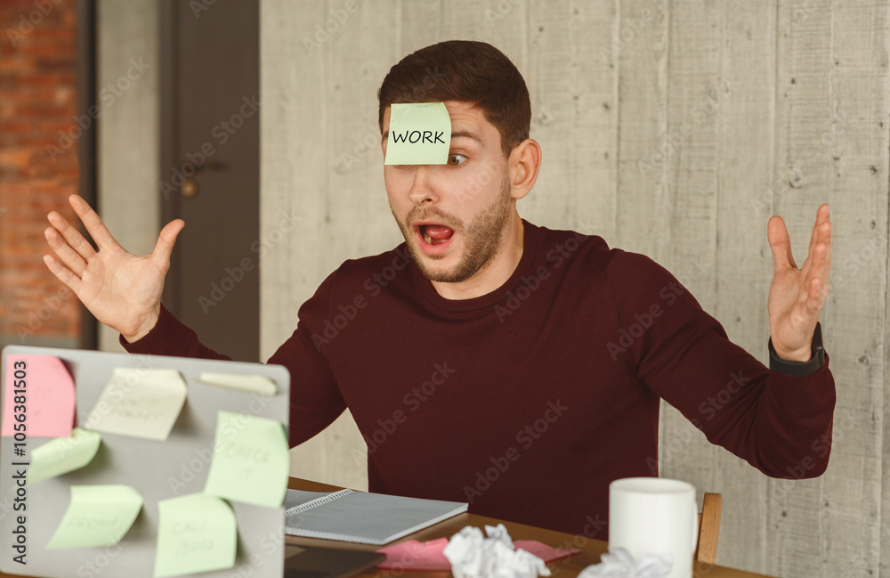 Poster overworked guy having sticky notes on laptop and face sitting in modern office. multitasking concept