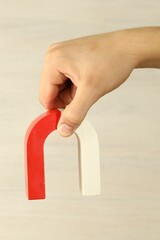 Man holding horseshoe magnet against light background, closeup