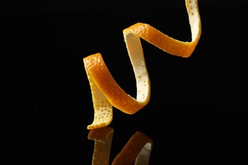 One fresh orange peel on black mirror surface, closeup