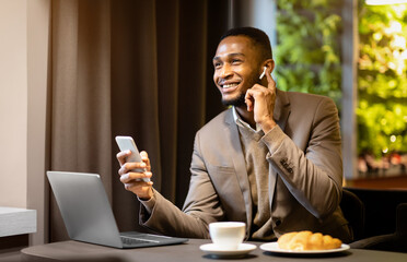 Hands Free Communication. Happy afro businessman speaking on mobile phone in headphones, touching...