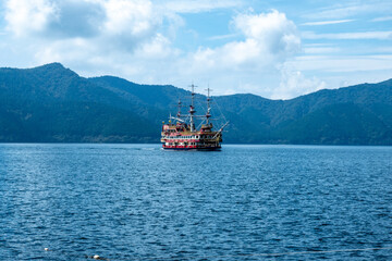 Fototapeta premium Red and black pirate ship sailing on lake ashi in hakone, japan, with mountains and blue sky in background