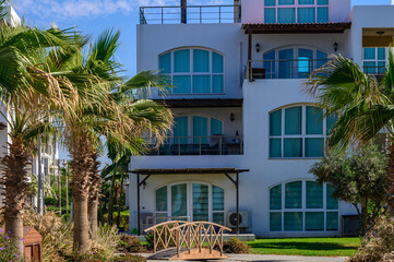 Fototapeta premium Tranquil resort building amidst lush palms and a charming wooden bridge in sunny coastal retreat