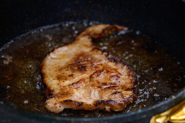 Sizzling pork chop cooking in a skillet with savory oil bubbling around it in a cozy kitchen setting