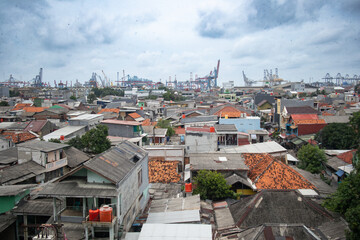 Obraz premium View over urban rooftops with industrial port and cranes in the background under cloudy skies