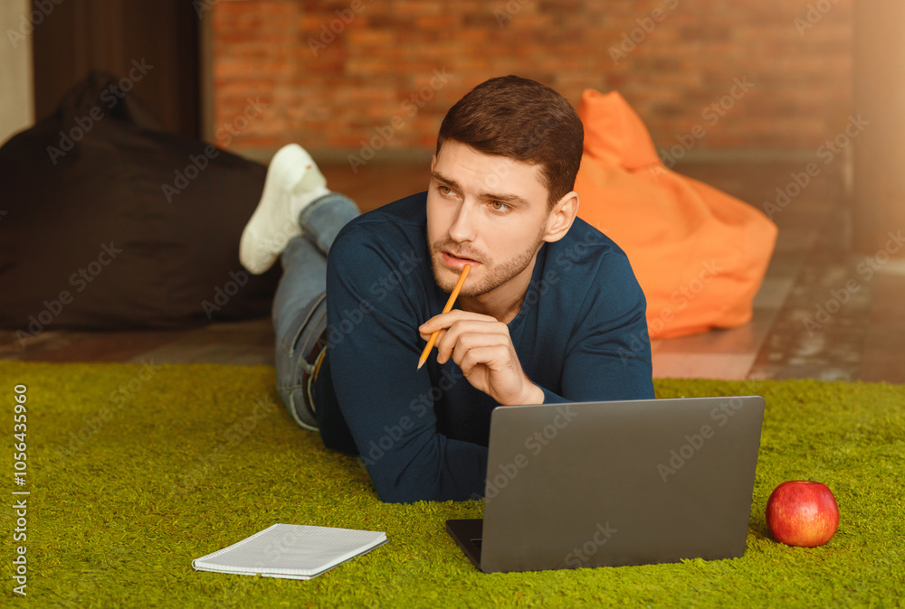 Poster Thoughtful Guy Using Laptop Thinking Creating Startup Lying On Floor In Modern Coworking Workspace. Creative Job And Freelance Lifestyle