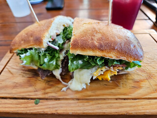 An Argentinean sandwich with lettuce and cheese on a wooden cutting board. The sandwich is cut in half and is placed on a table