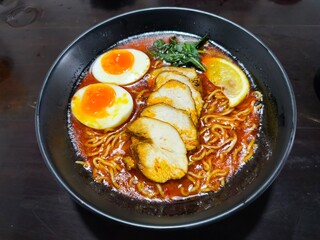 A bowl of spicy chicken ramen topped with delightful chicken chashu, ajitsuke tamago, and a slice of lemon.
