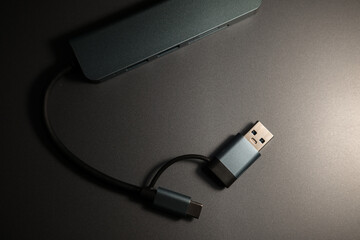 A compact, gray USB-C hub with multiple ports and attached cables, resting on a metallic surface...