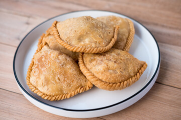 Indonesian kue pastel goreng are deep-fried pastries with a crimped edge, filled with savory mixtures, featuring unique texture and cultural significance. Served on a plate.