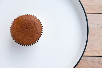 chocolate cupcake on white ceramic plate, placed on a wooden surface.