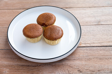 chocolate cupcake on white ceramic plate, placed on a wooden surface.