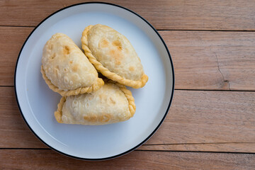 Golden, flaky curry puffs rest warmly on a simple white plate, radiating a cozy, rustic charm against the wooden table backdrop.