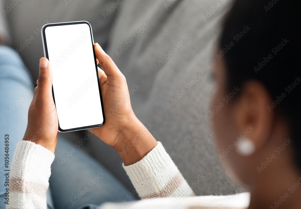 Aufkleber unrecognizable black woman holding smartphone with white screen at home, over shoulder view of afric