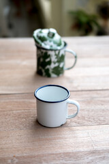 Two enamel mugs on a wooden surface. 