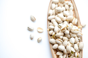 A light-colored basket filled with pistachio nuts, some scattered on a white surface. The pistachios, in their shells with some slightly open, reveal the green nut inside, showcasing a nutritious snac