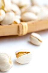 Close-up of several pistachios, some shelled and some still in their partly opened shells, arranged near a light wooden element on a white surface. Fresh and natural snack.