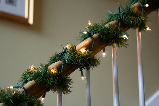 Golden Christmas lights and green garland wrapped around staircase railing