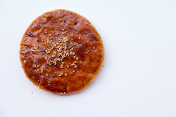 Round, golden-brown Chinese Sweet Pie (Laobing), glazed and sprinkled with sesame seeds on a white surface. A simple and sweet pastry.