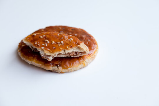 Round, golden-brown Chinese Sweet Pie (Laobing), partially broken to reveal the filling, sprinkled with sesame seeds on a white surface. A simple and sweet pastry