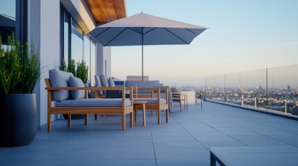 Fototapeta premium Stylish modern balcony with wooden furniture and large umbrella overlooking the city skyline at sunset.