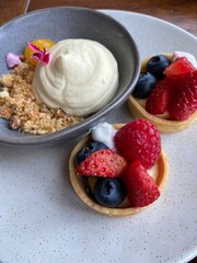 Berry fruit tarts and mascarpone cheesecake served on the white plate on the wooden table 