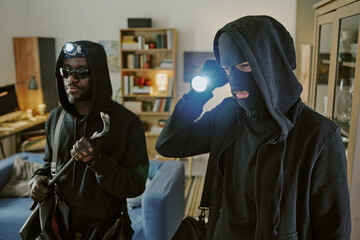 High angle of thieve in black clothes using flashlight while seeing living room