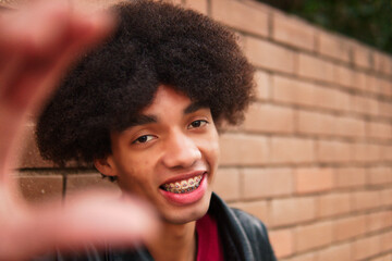 Dark-skinned Latino boy with braces and afro, playing and posing, against a brick wall background in the city. having lots of fun and fooling around