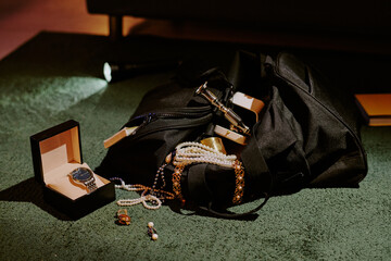 Huge black bag full of golden accessories and jewelry on deep green carpet