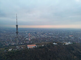 Fototapeta premium Koktobe TV tower on a hill at sunset, against the background of the city. Cloud cover. Autumn. The view from the drone.