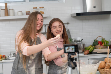 Happy mother showing star cookies to live streaming video while preparing bakery with teen daughter in the kitchen. Family enjoy cooking together on weekend