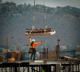 Eye level view of a construction worker guiding a load from a crane at a large commercial building...