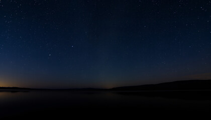 Fototapeta premium Starry night sky over a calm lake, with stars reflecting on the water surface, creating a tranquil atmosphere.