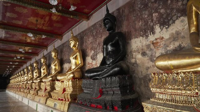Black Buddha statue among a row of many golden statues sitting in a meditative pose in the courtyard of a Buddhist temple Wat Pho. The most visited tourist place in Bangkok, Thailand
