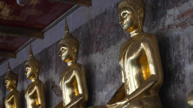 A row of many statues of a gold Buddha sitting in a meditative pose in the courtyard of a Buddhist temple Wat Pho. The most visited tourist place in Bangkok, Thailand