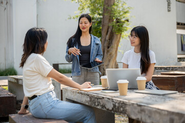 A smart Asian female college student is tutoring math to her friends at a table in a college park.