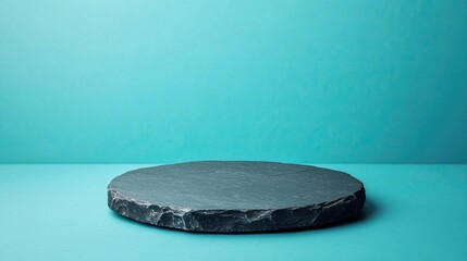 A circular black slate plate on a turquoise background, creating a minimalist aesthetic suitable for presentation or display.