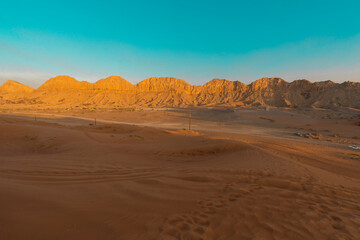 Fototapeta premium layer of desert mountains during winter in the deep desert with golden sand dunes. blue sky in the horizon foot markings in sand during golden hour adventurous desert safari