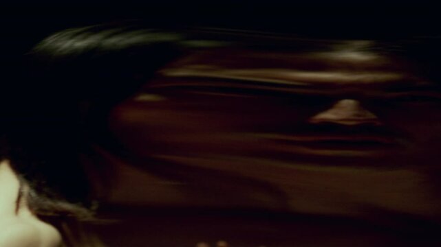 Young long-haired man with shirtless torso moving in dark studio in front of distorting mirror, his warped reflection creating eerie atmosphere