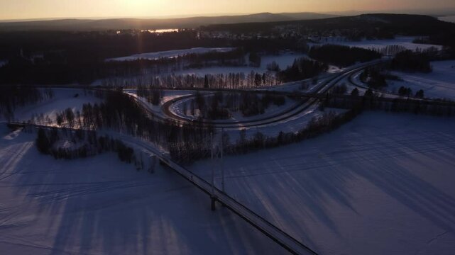 Aerial view over a cable-stayed bridge with a highway in the background slowly tilting up revealing a beautiful winter sunset in northern Sweden