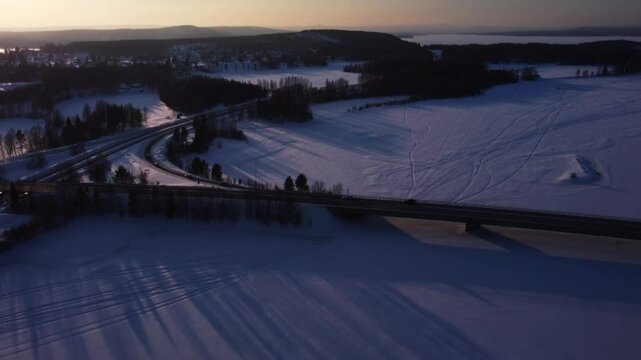 Traffic driving on a highway bridge over a frozen lake during a beautiful winter sunset in northern Sweden