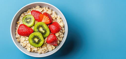 A bowl of oatmeal topped with fresh strawberries and kiwis on a vibrant blue background.