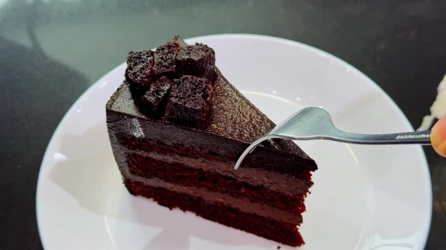 Chocolate fudge cake with chocolate glaze sauce on a plate, taking bite with a fork. Closeup view
