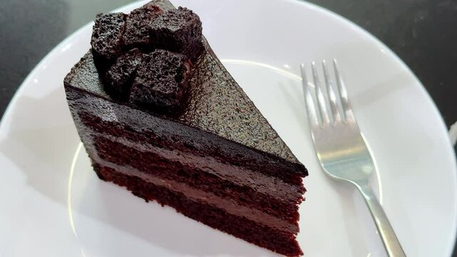 Chocolate fudge cake with chocolate glaze sauce on a plate, taking bite with a fork. Closeup view