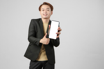 portrait of happy asian businessman wearing suit holding mobile phone and showing blank screen  giving thumb up gesture on isolated background.