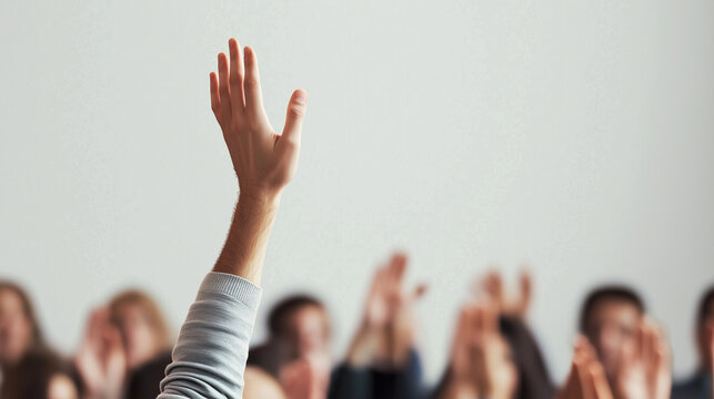 A hand is raised among a blurred audience, symbolizing participation, question-asking, or engagement in a seminar or educational setting.