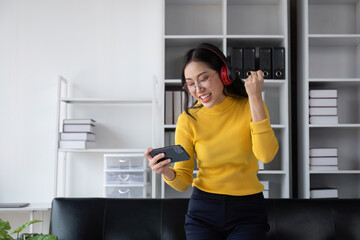 Beautiful Girl Celebrating with Joy, Wearing Headphones and Smiling While Holding a Smartphone in a Modern Office Setting