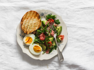Delicious breakfast, snack - boiled egg and tuna, avocado, tomatoes, arugula salad on a light background, top view