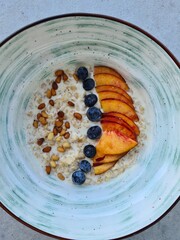 Colorful breakfast bowl with oatmeal, peaches, blueberries, and pine nuts arranged creatively on a rustic plate