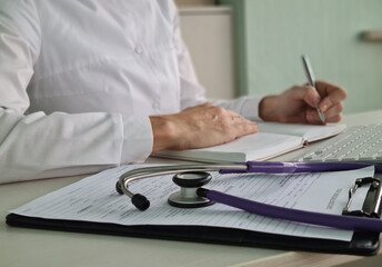 Healthcare professional taking notes at a desk with a stethoscope and medical documents 