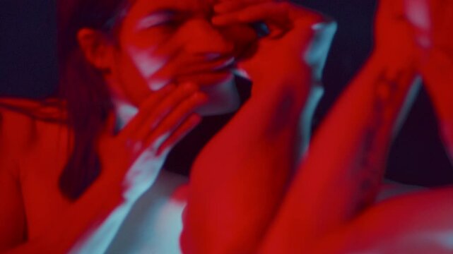 Warped surreal reflection of insane man grasping his face with hands and opening mouth in front of distorting mirror, in dark studio illuminated in red and blue lighting